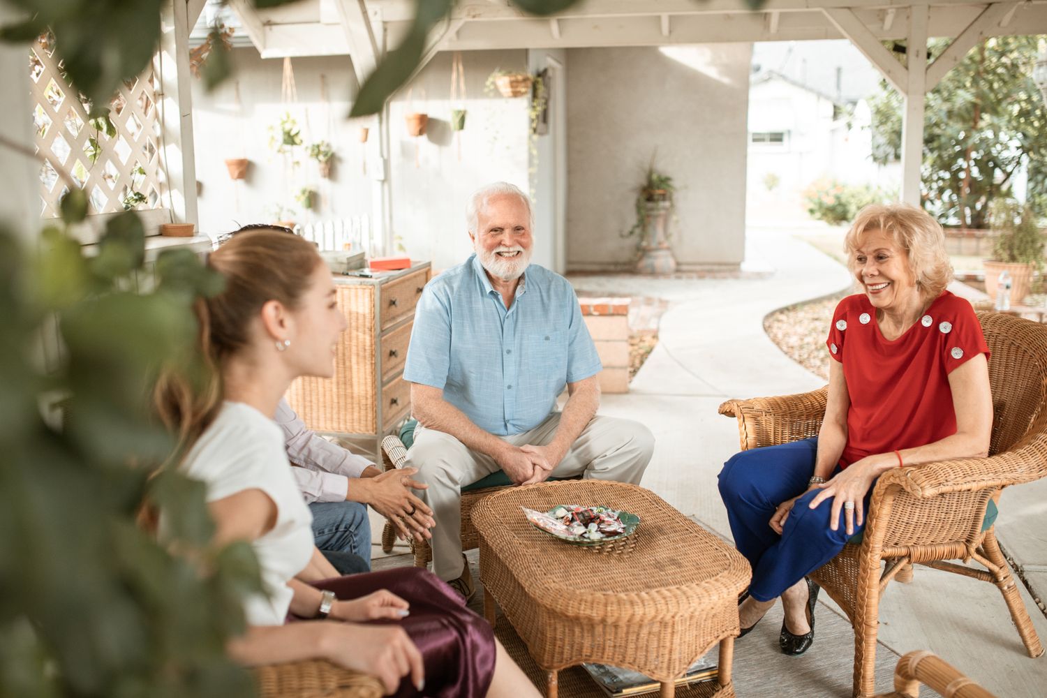 A teenage girl laughing with her grandmother and grandfather on a sunny covered patio.